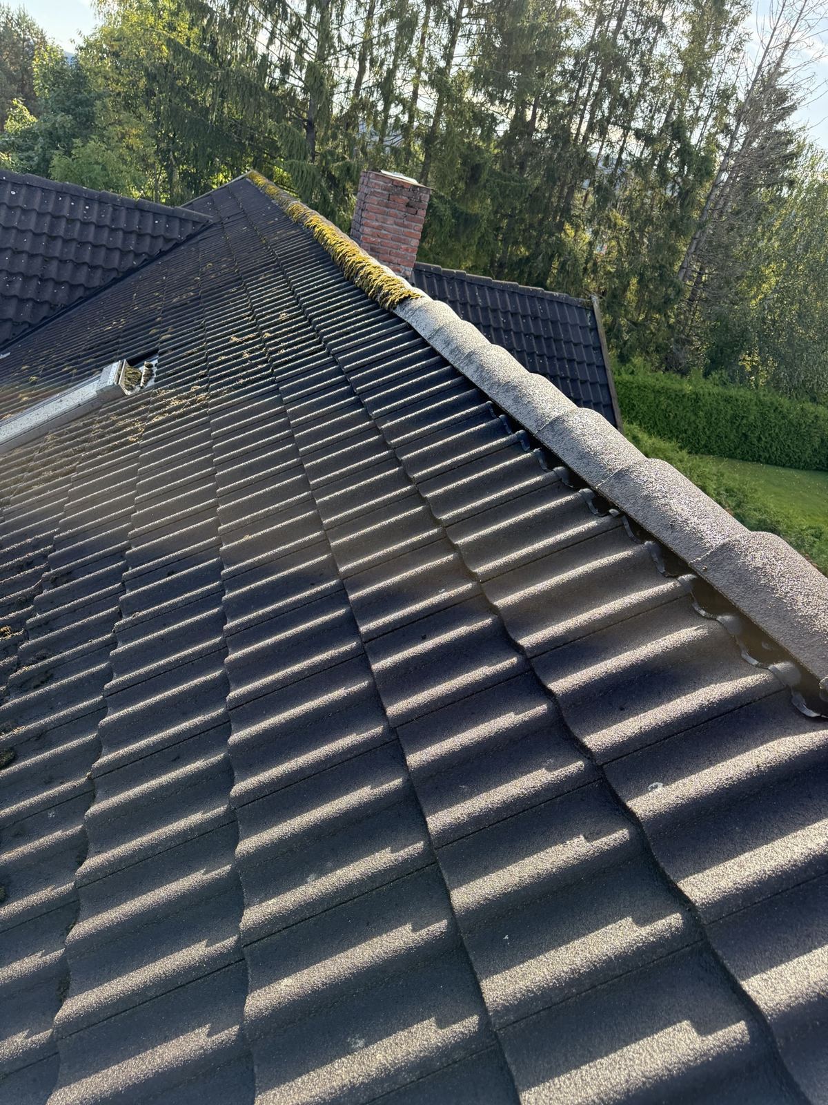 Renset mørkt tak med mose igjen langs mønet og en teglpipe
